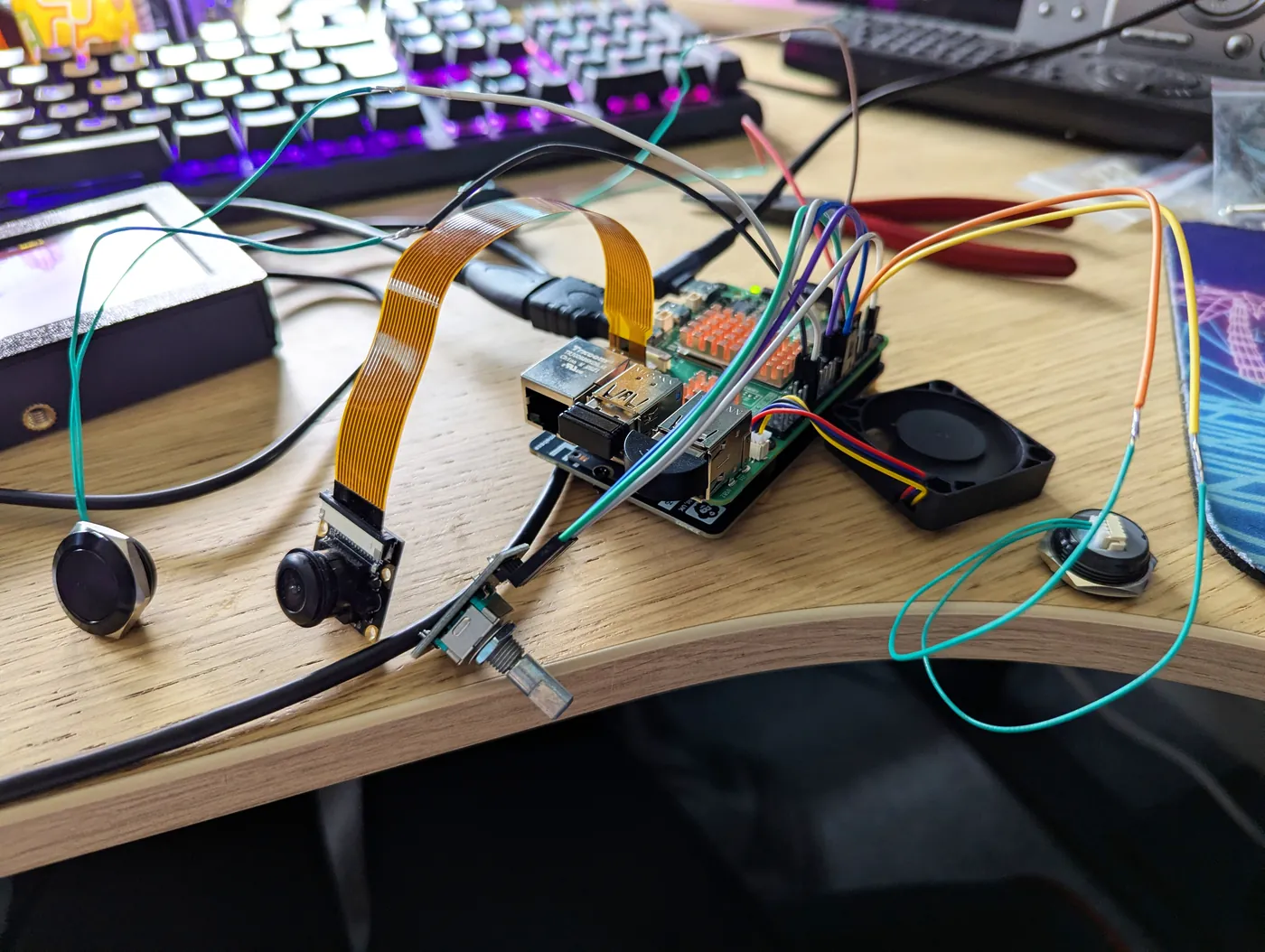 A Raspberry Pi wired to a camera module, buttons and a rotary encoder on a desk